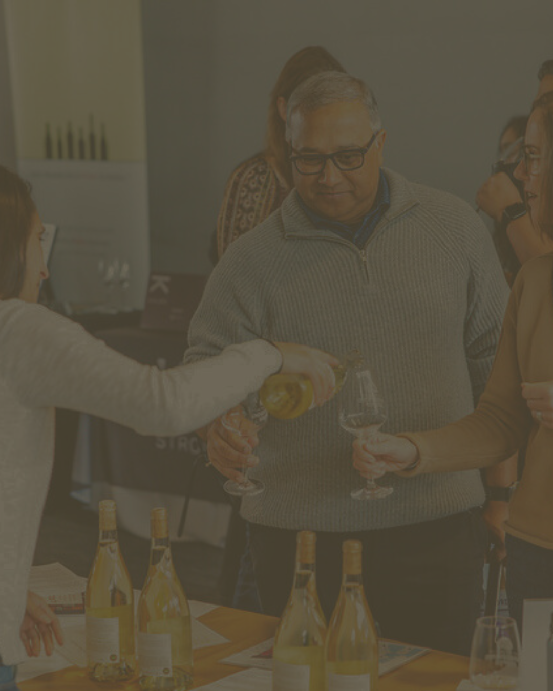 Guests having white wine poured into their glasses at an indoor tasting event.