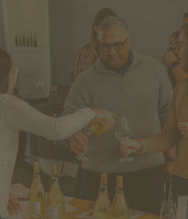 Guests having white wine poured into their glasses at an indoor tasting event.